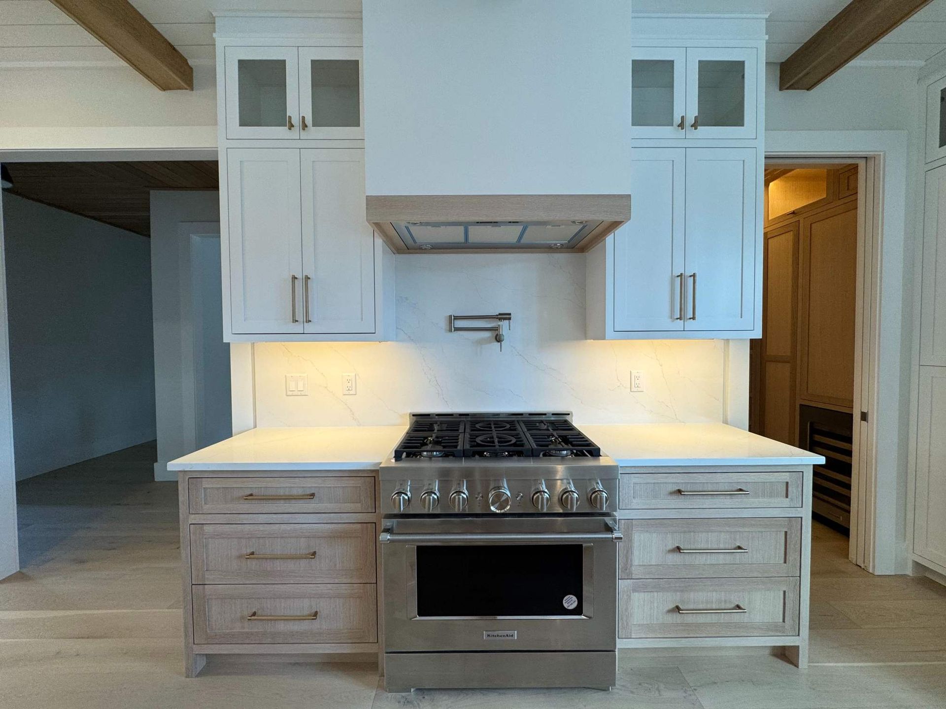 Kitchen with stove, cabinets, and light wood beams. Stainless steel appliances and light countertops.