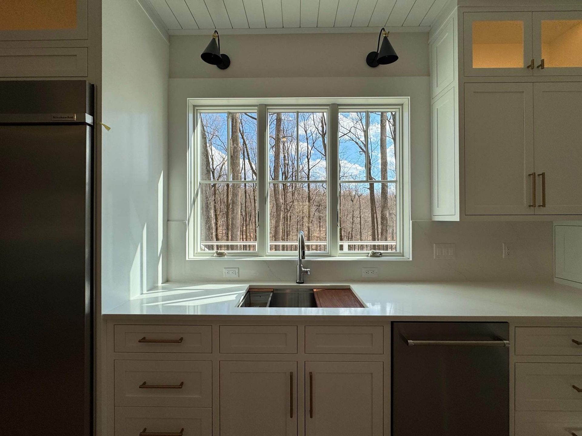 Kitchen with white cabinets, stainless steel appliances, and a window with a forest view.