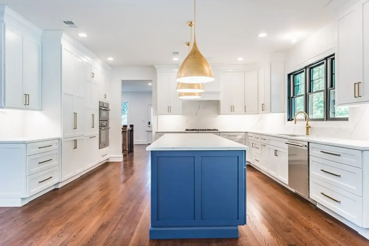 Modern white kitchen with blue island, gold pendant lights, and wood floors.