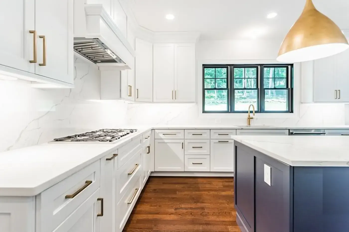 White kitchen with navy island, hardwood floors, gold accents, and a window.
