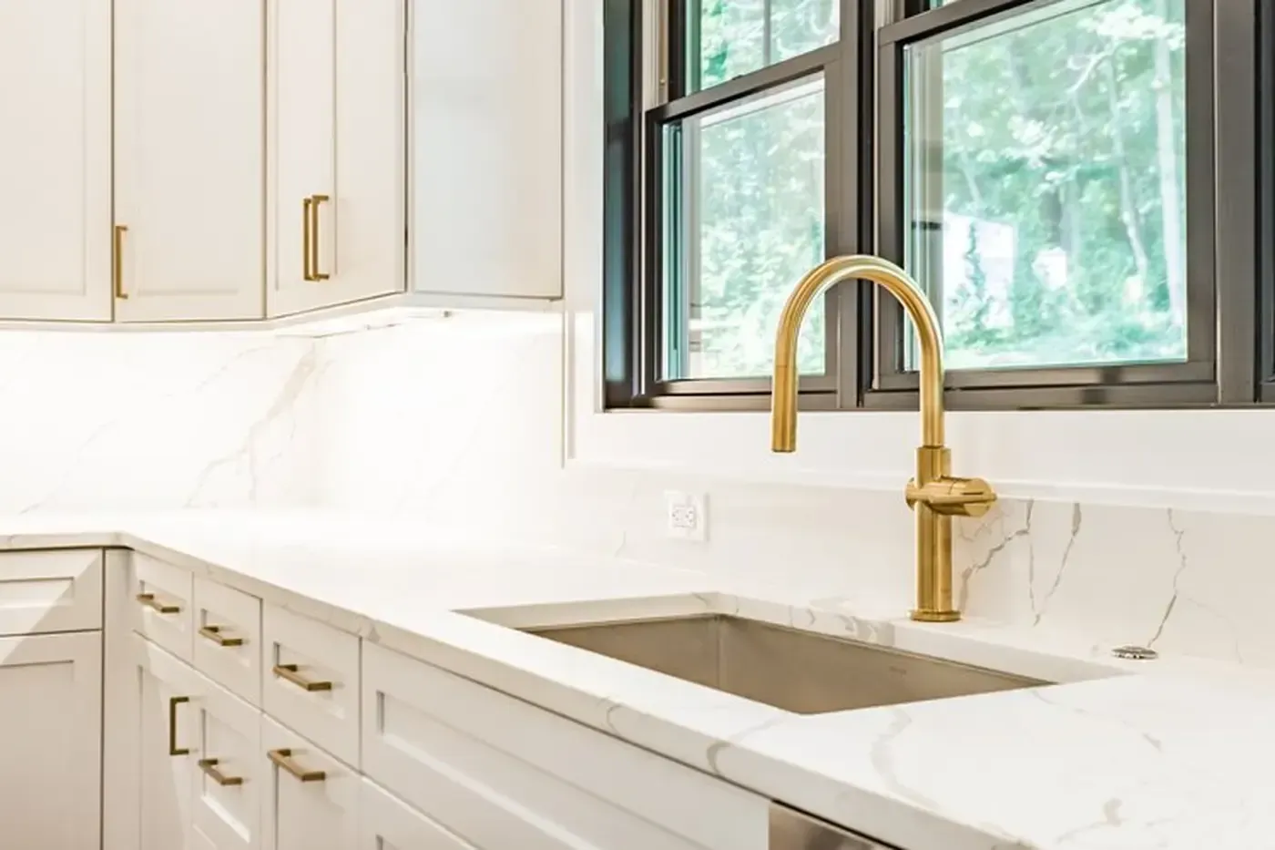 Kitchen with white cabinets, marble countertops, gold faucet, and a window with a view.