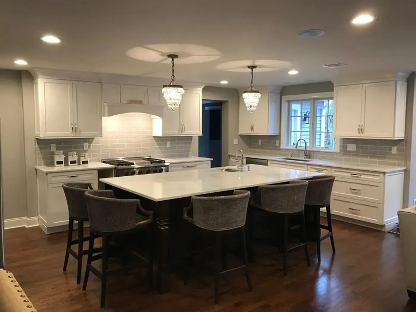 Elegant white kitchen with island, marble countertops, and pendant lights. Bar stools and dark wood floors.