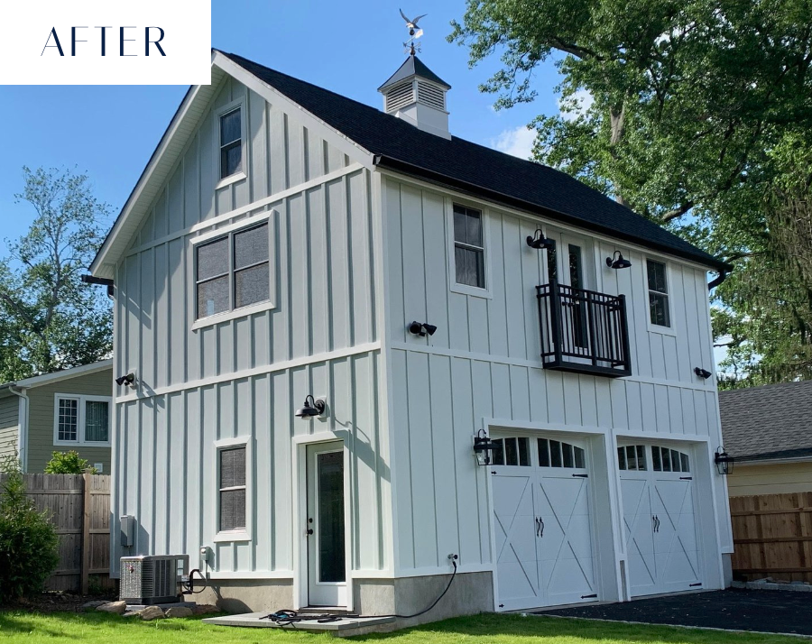 Two-story barn-style building with white siding, black roof, and two garage doors under blue sky.
