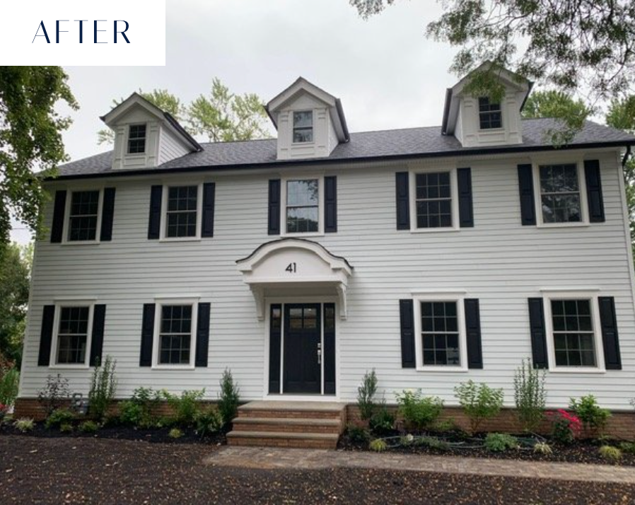 White house with black shutters and door, three dormer windows, landscaped front yard.