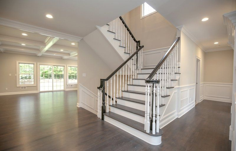 A foyer with dark wood floors, white wainscoting, and a staircase featuring dark treads and white railings.