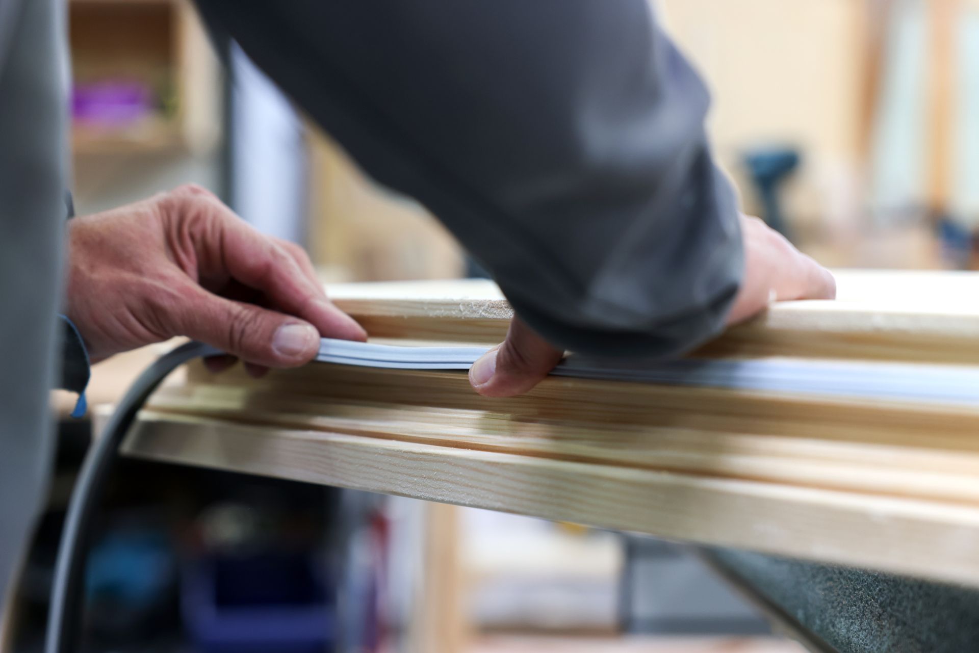 Une personne perce un trou dans une planche de bois à l'aide d'une perceuse électrique, à l'intérieur.