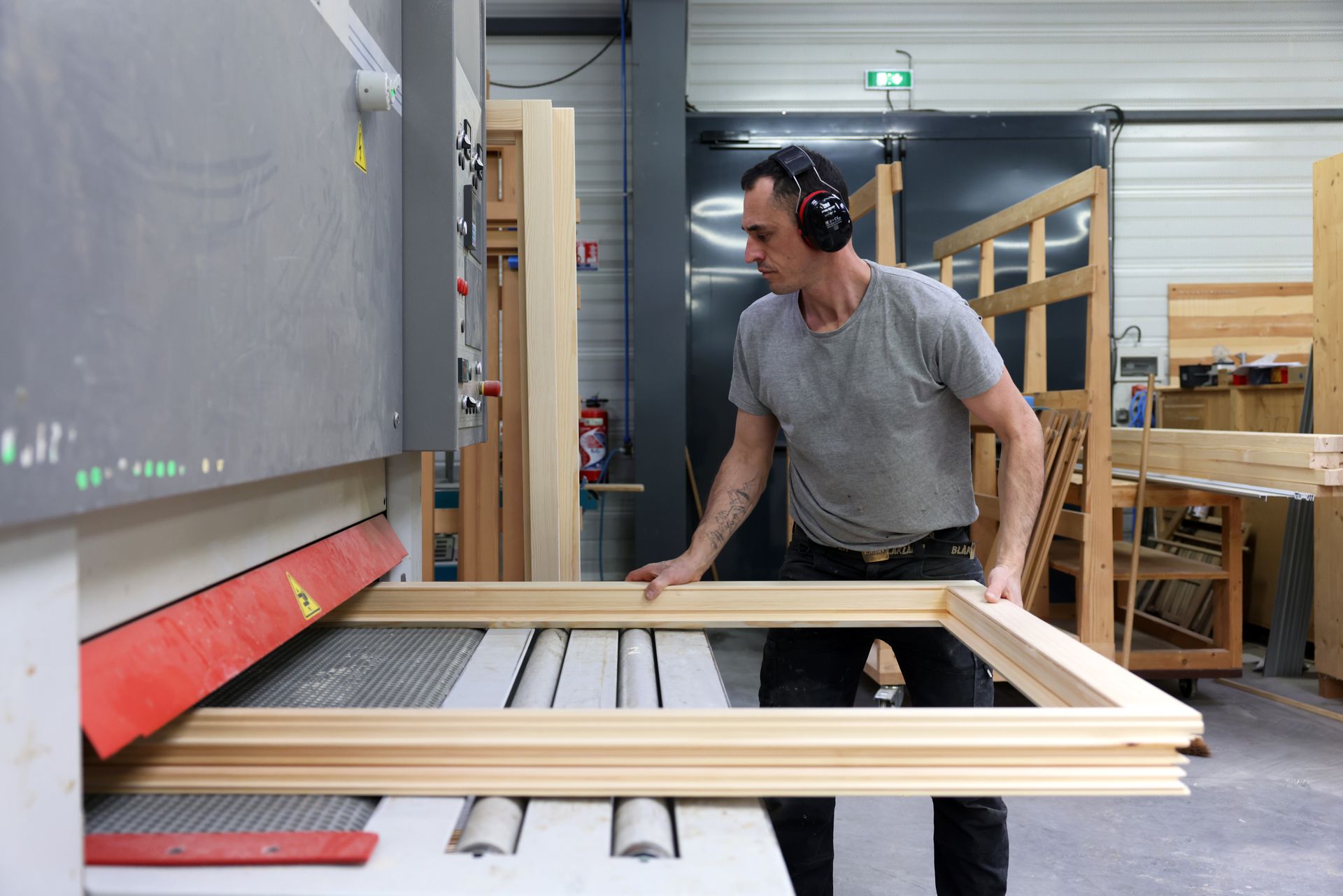 Un menuisier inspecte du bois sur un établi, portant des lunettes de sécurité et des gants.