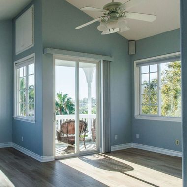 Pièce vide aux murs bleus, porte coulissante en verre donnant sur un balcon et lumière naturelle.