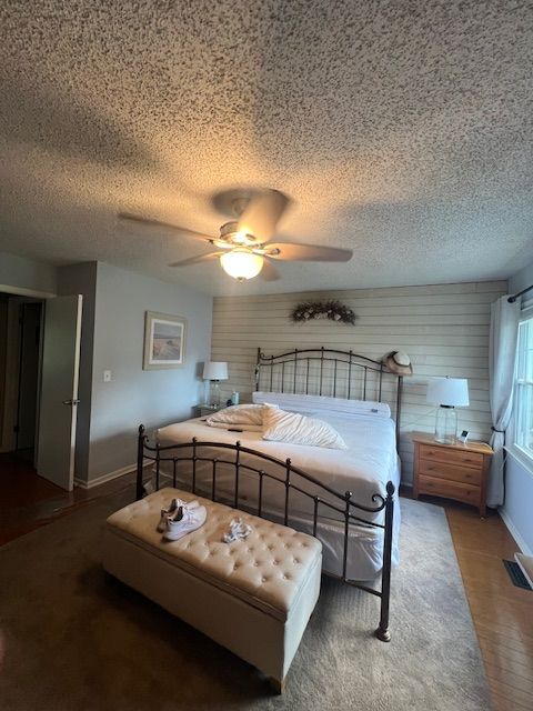 Bedroom with a large bed, bench, ceiling fan, and wooden furniture against light-colored walls.
