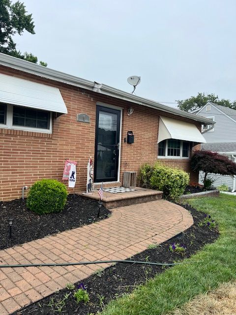Brick house with a red brick path leading to a black door. Beige awnings over windows.