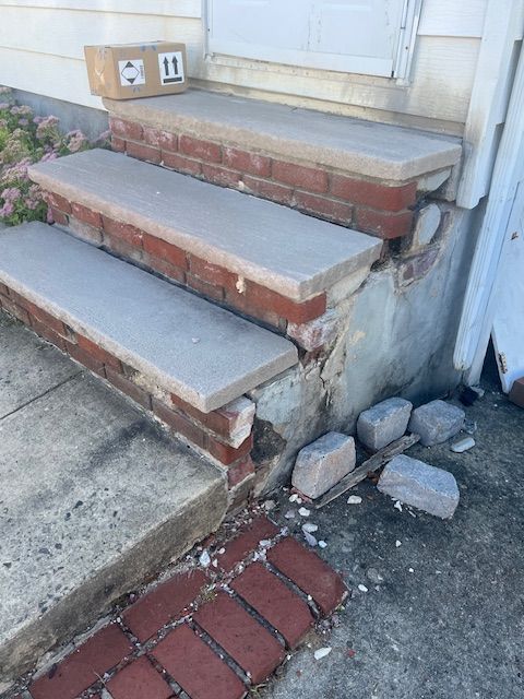 Damaged brick steps leading to a white door. Concrete and brick are crumbling; a package sits at the top.