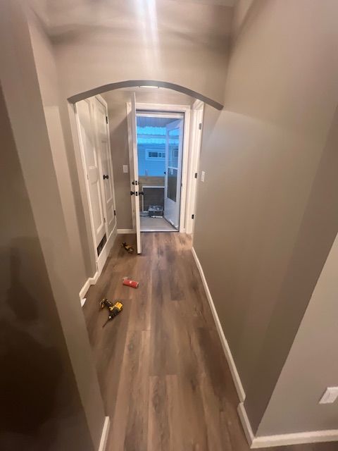 Narrow hallway with brown wood-look flooring and gray walls. A doorway leads outside, with two white doors on the left.
