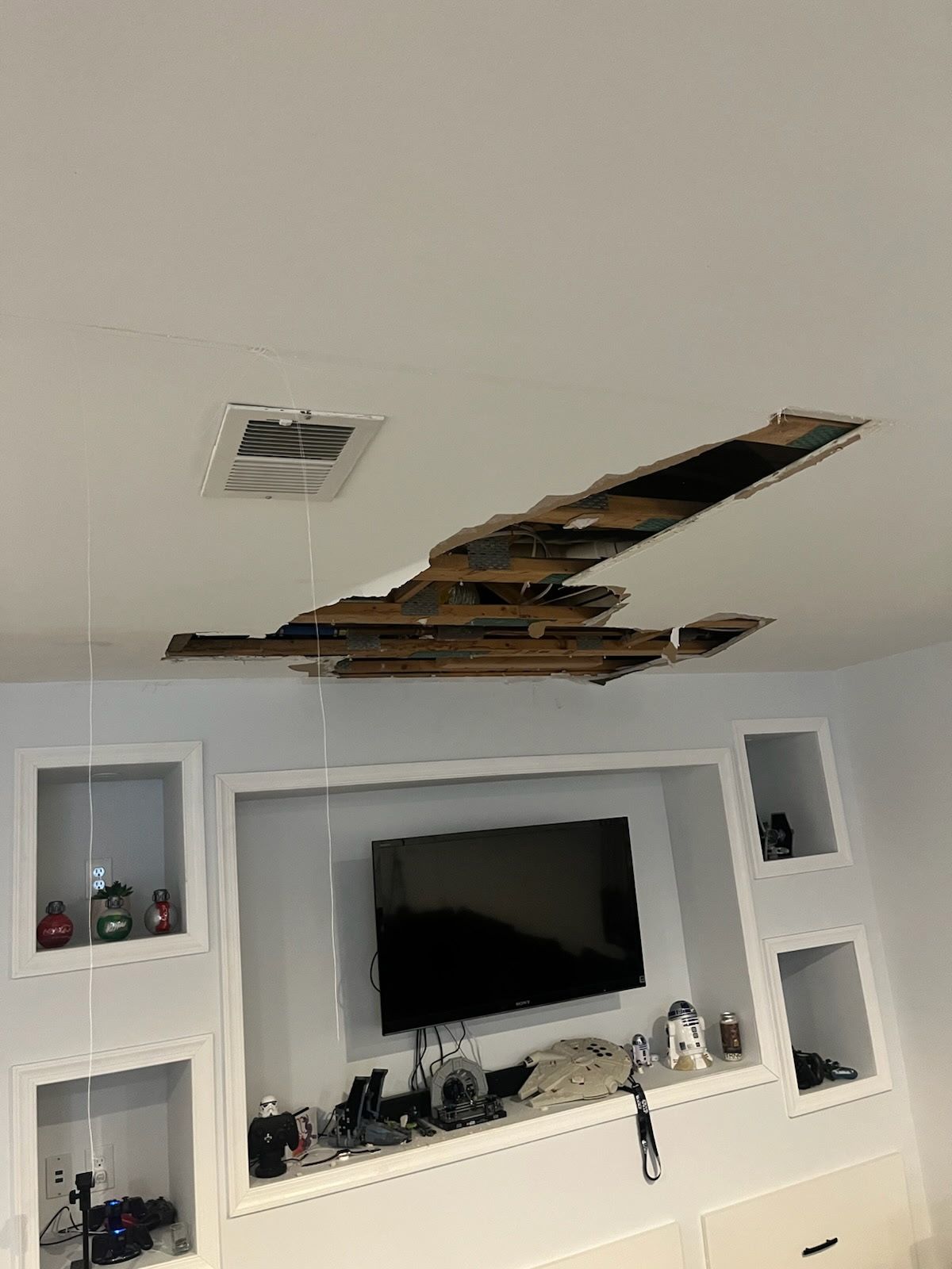 Damaged ceiling with a large hole over a built-in entertainment center with a TV and recessed shelves.