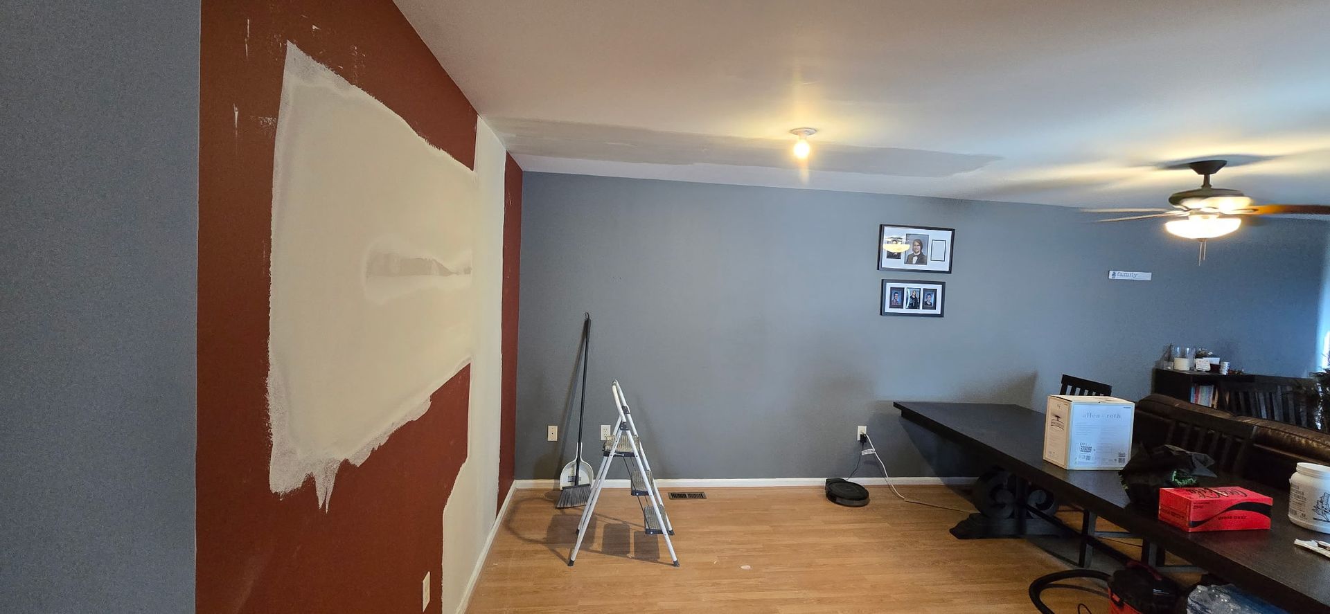 Room with walls being painted; a ladder and a long table are present.