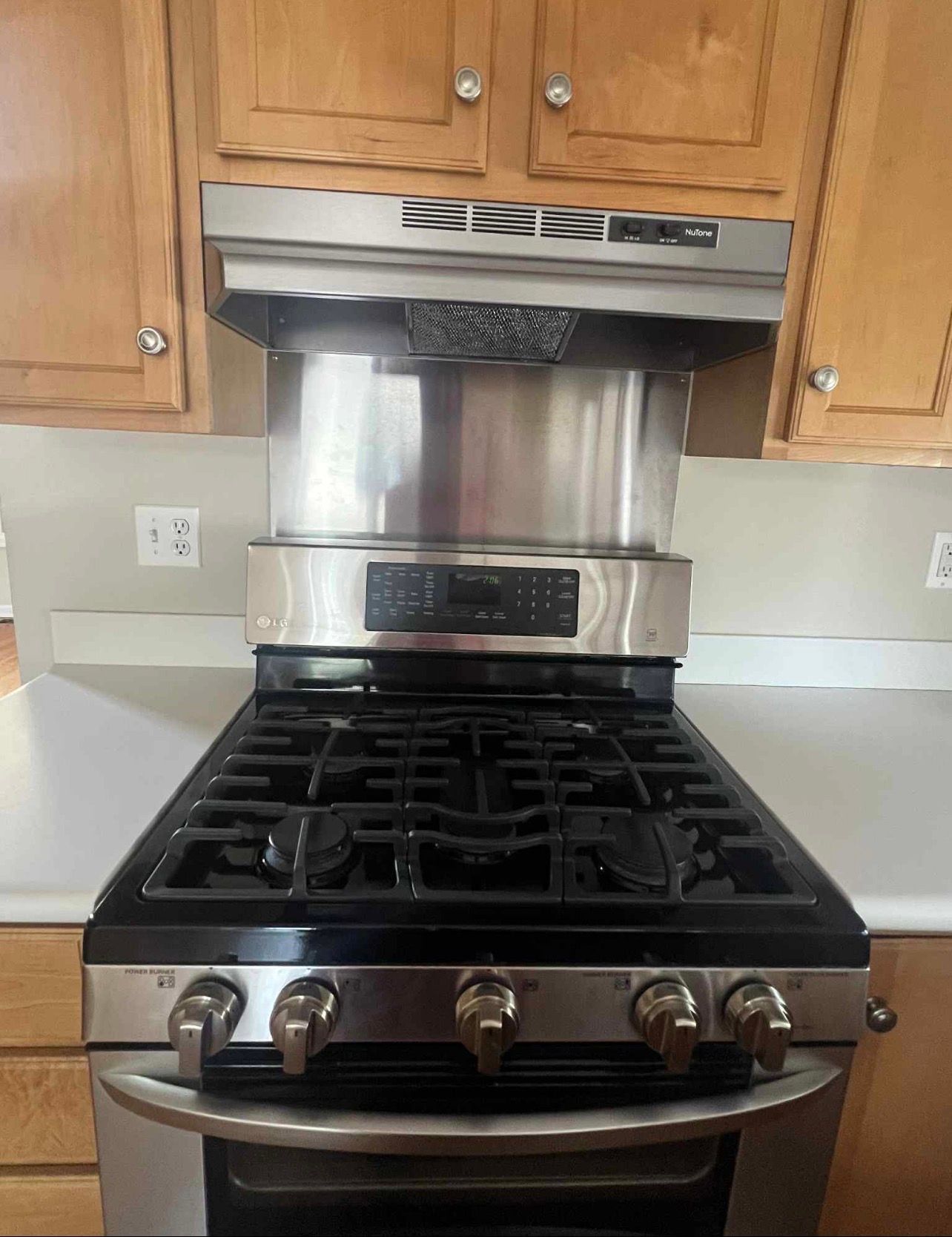 Stainless steel gas stove with a black cooktop and matching range hood in a kitchen.