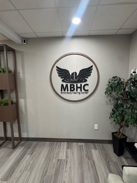 MBHC sign on a grey wall with a circular logo, surrounded by plants and grey flooring.