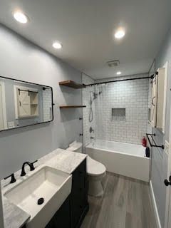 Bathroom with white subway tile shower, gray wood-look floor, black fixtures, and a white sink.