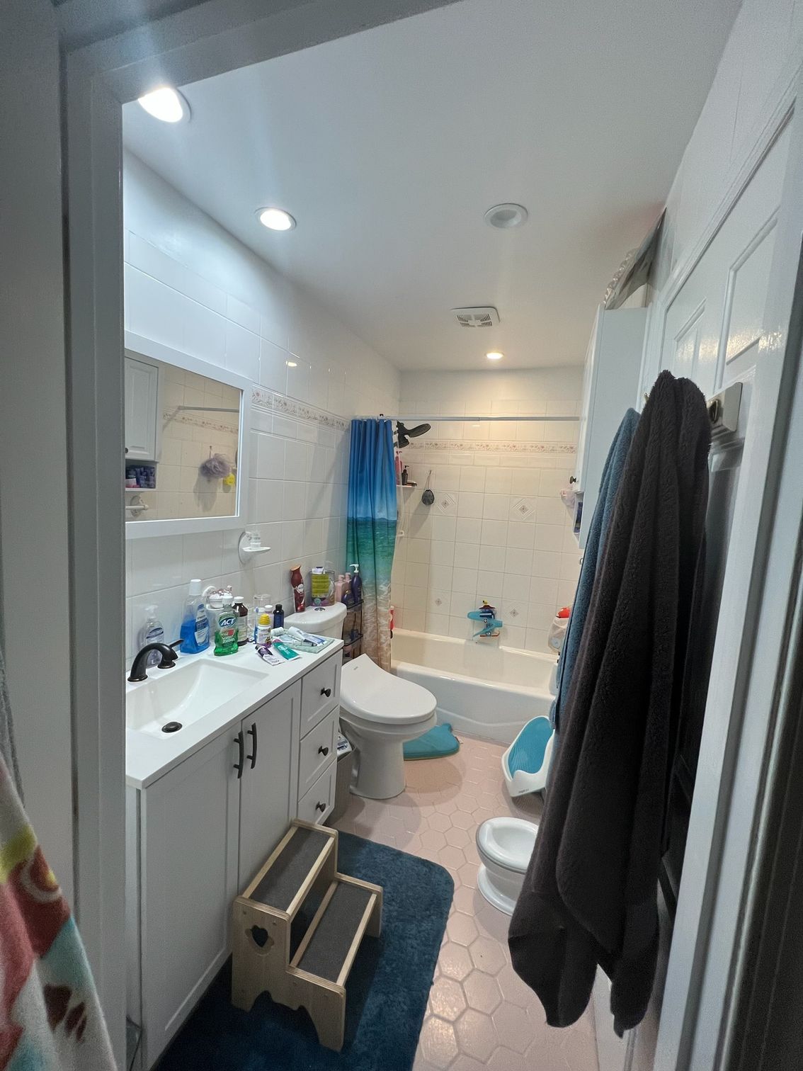 Small bathroom with a white vanity, toilet, and bathtub; blue and pink accents.