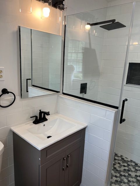 Small modern bathroom with gray vanity, black fixtures, glass shower, and white subway tile.