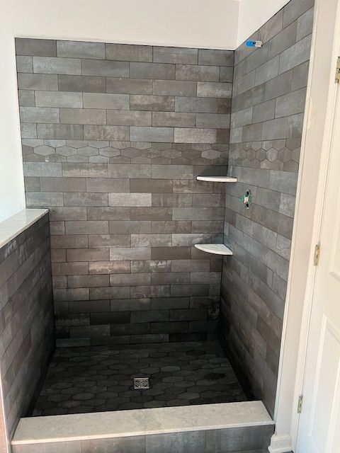 Gray tiled shower stall with two corner shelves.