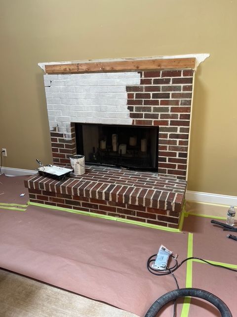 Fireplace being painted white, partially completed, with brown brick and wood trim.