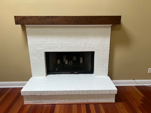 White painted brick fireplace with dark brown wooden mantle, dark interior and hearth on wooden floor.