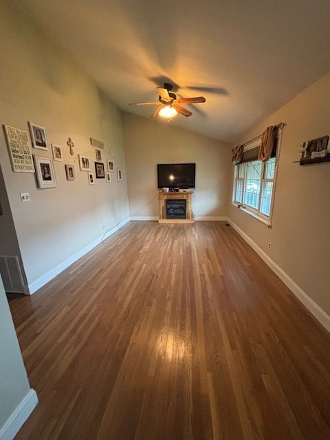 Living room with hardwood floors, TV above fireplace, decorative wall art, and window with brown valance.