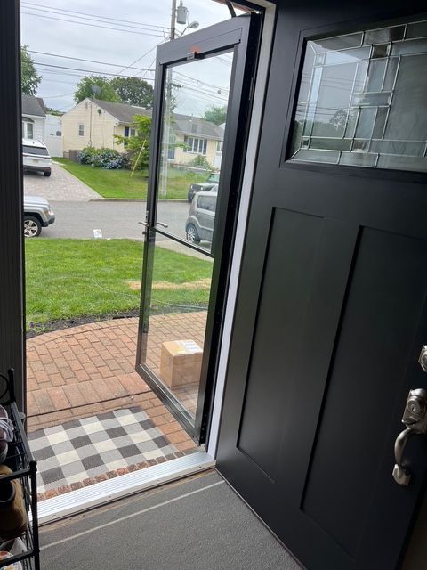 Black front door open to reveal a screen door and suburban street, package on the doormat.