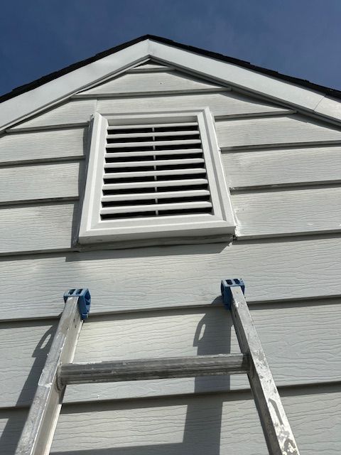 White siding on a building with a vent and ladder. Blue sky in background.