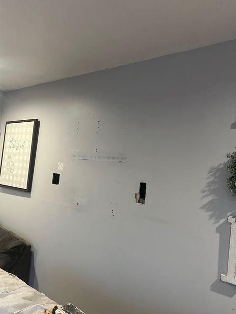 Gray wall with patching, electrical outlets, and a framed print.