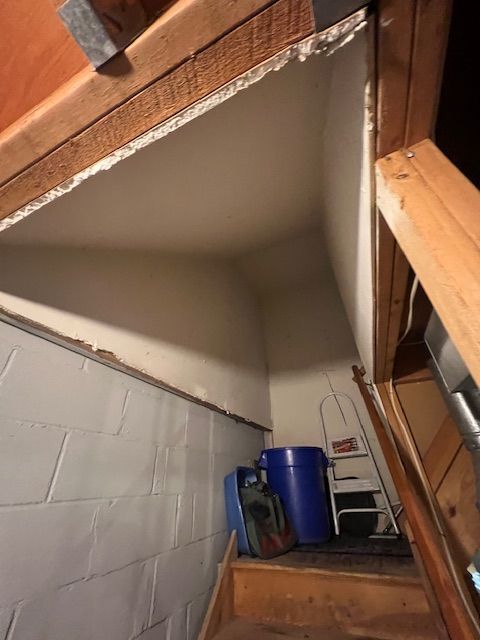 Staircase leading up, revealing an unfinished space with white walls and a blue barrel.