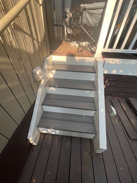 Wooden deck stairs leading down. Gray treads, white risers, railing on one side.