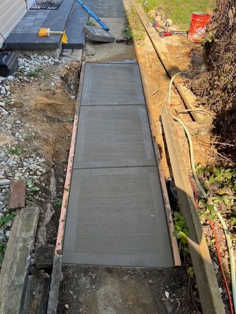Newly poured concrete sidewalk with wooden forms in a residential yard.