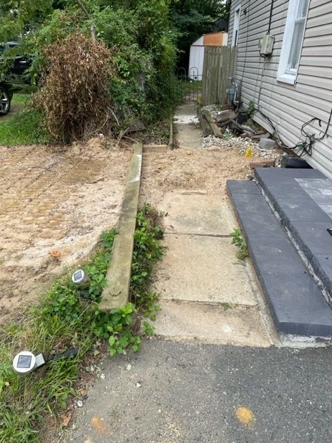A gravel pathway with concrete sections leading alongside a house and to a shed in the distance.