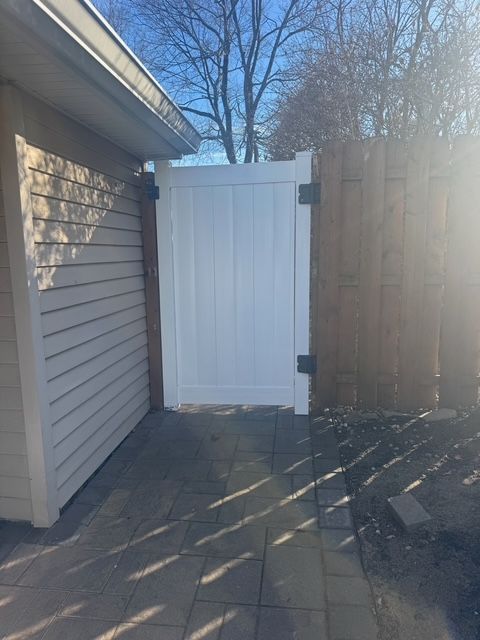White gate in a wooden fence and beige building corner on a brick patio.