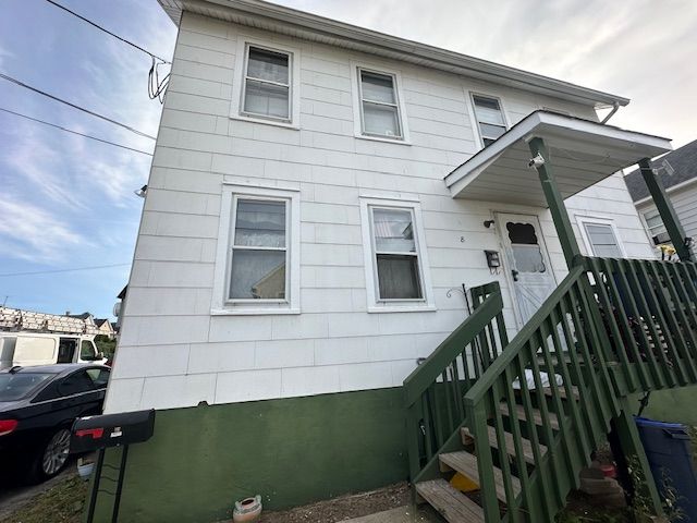 White two-story house with green foundation and stairs leading to front door; a car is parked on the left.