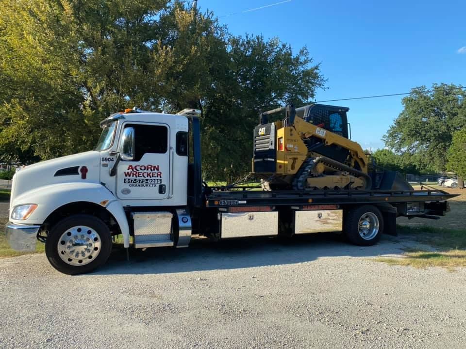 A tow truck with a bulldozer on the back is parked in a gravel lot.