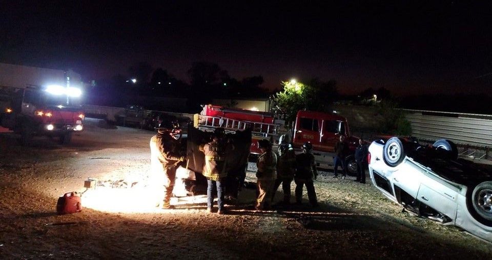A group of firefighters are standing next to a car that is on its side.