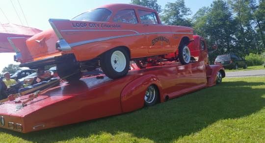 An orange car is sitting on top of a red trailer.