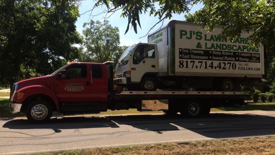 A tow truck is carrying a pj 's lawn care and landscaping truck.