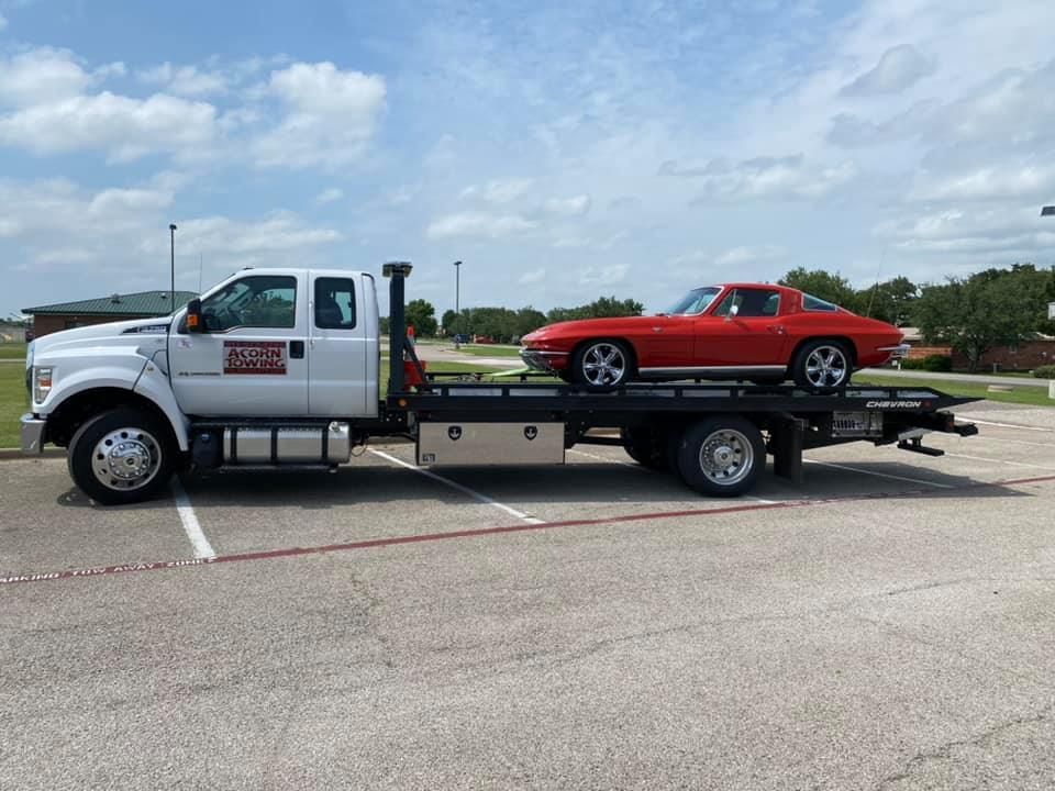 A red corvette is being towed by a tow truck.