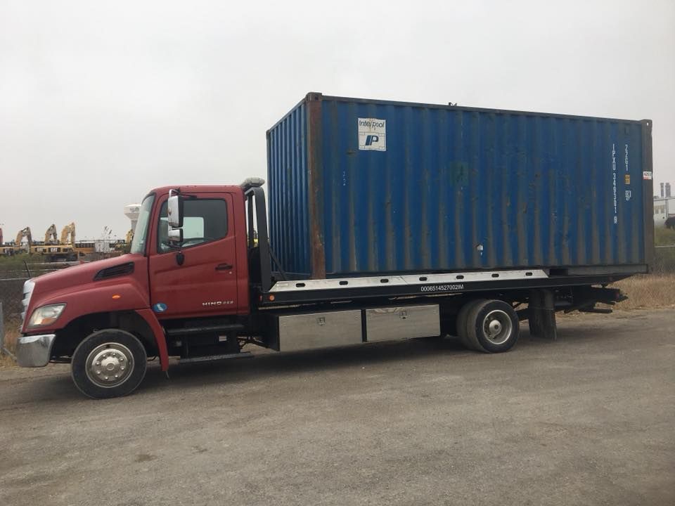 A red tow truck is carrying a blue shipping container.