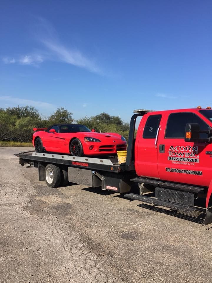 A red tow truck is towing a red sports car.