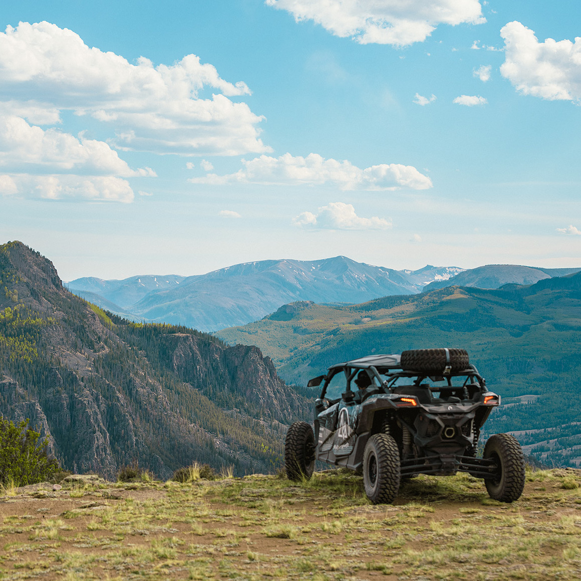 Black off-road vehicle parked on a mountain ridge with a scenic view of mountains and a blue sky.
