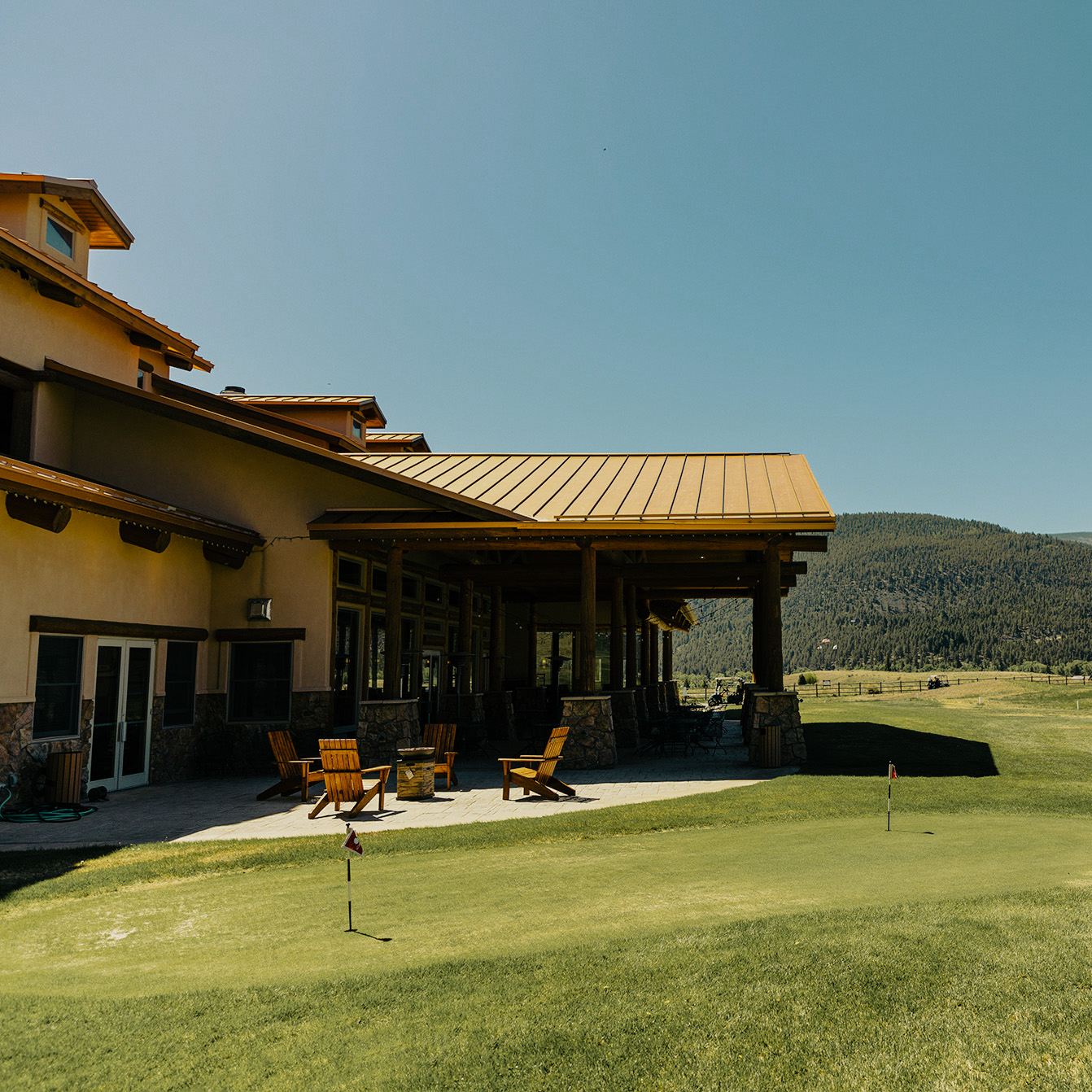 Golf course clubhouse with a patio and lawn, on a sunny day.