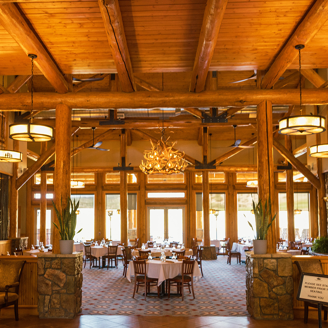 Dining room with wood beams, stone columns, and tables set for a meal.