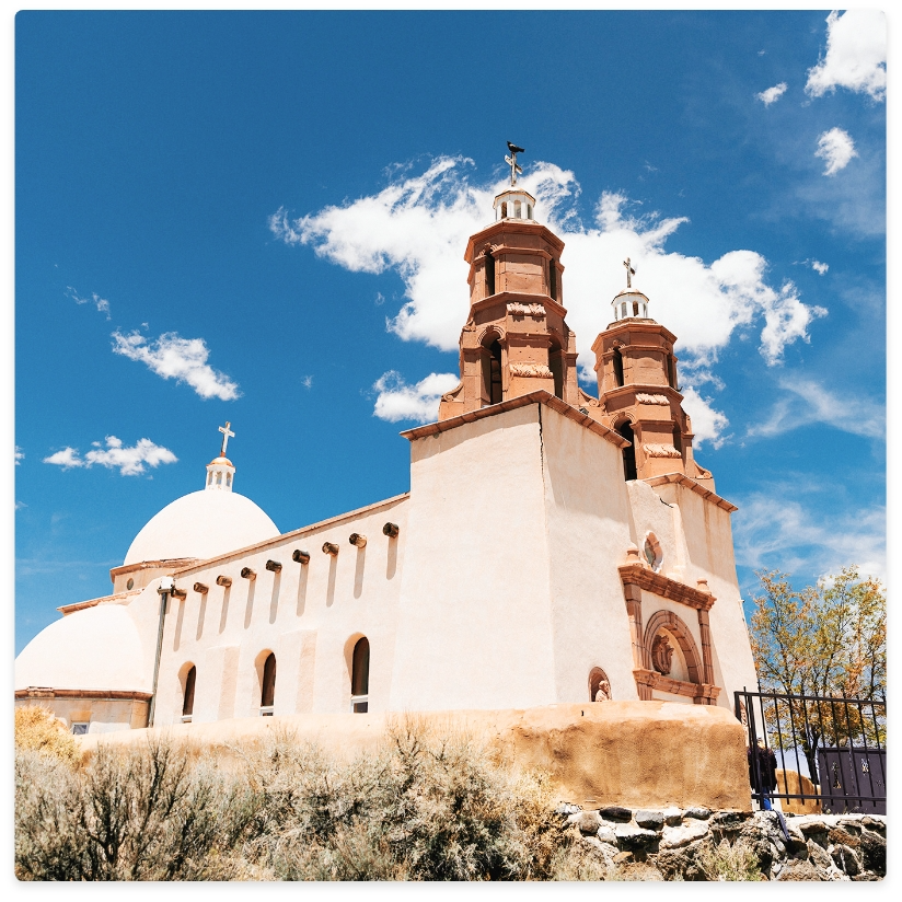 Cream-colored church with red-brown bell towers under a blue sky with clouds.