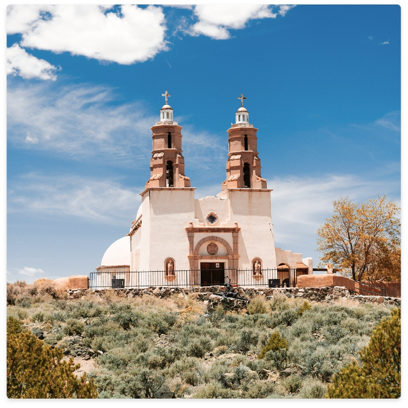Tan church with twin bell towers on a hilltop under a blue sky.