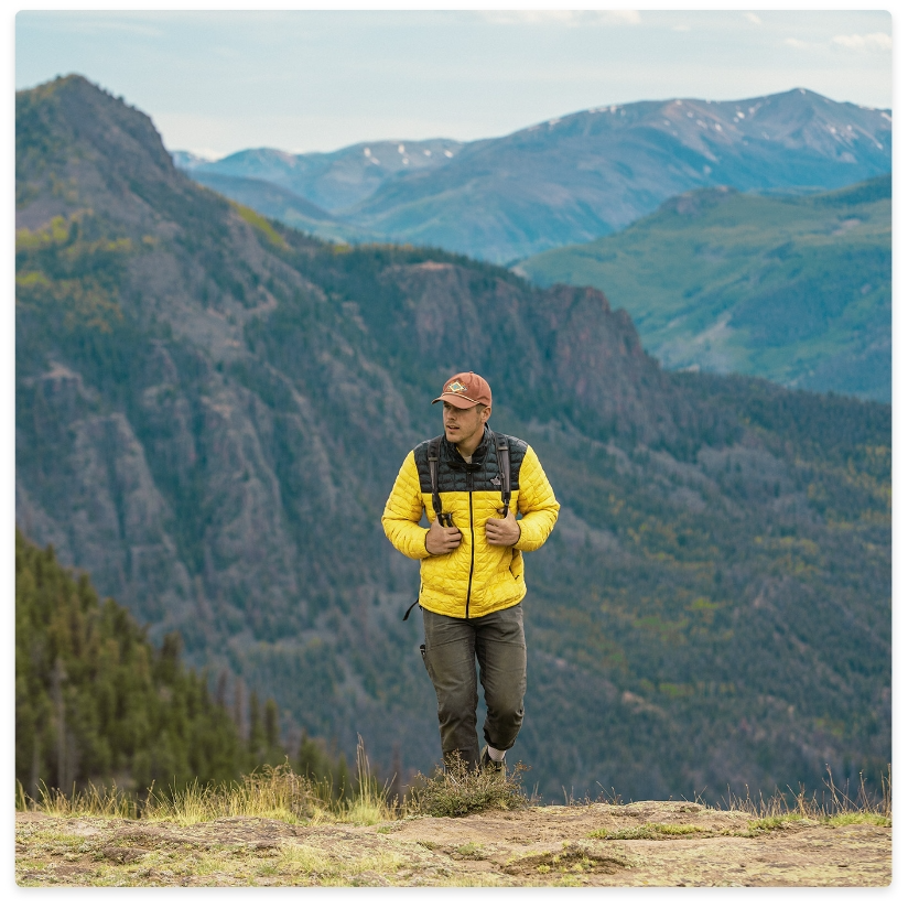 Man in yellow jacket hikes in mountains.