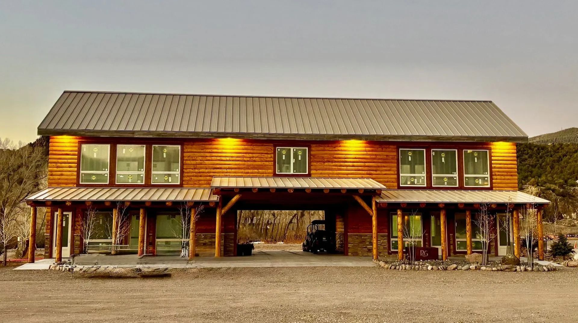 Rustic two-story wooden lodge with a covered porch and many windows in a gravel clearing